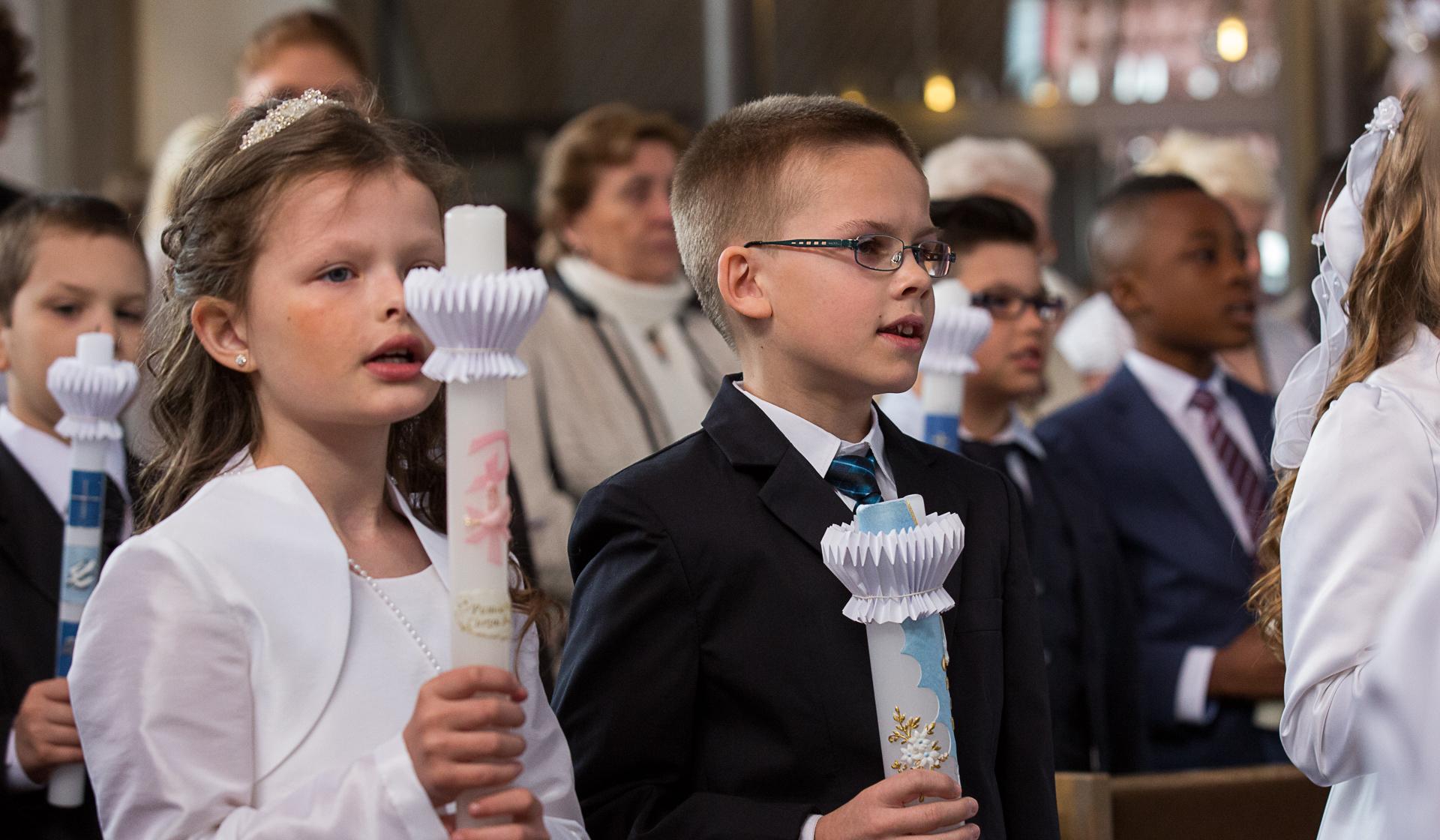Mehrere Kinder in festlichen Kleidern mit einer Kerze in der Hand.