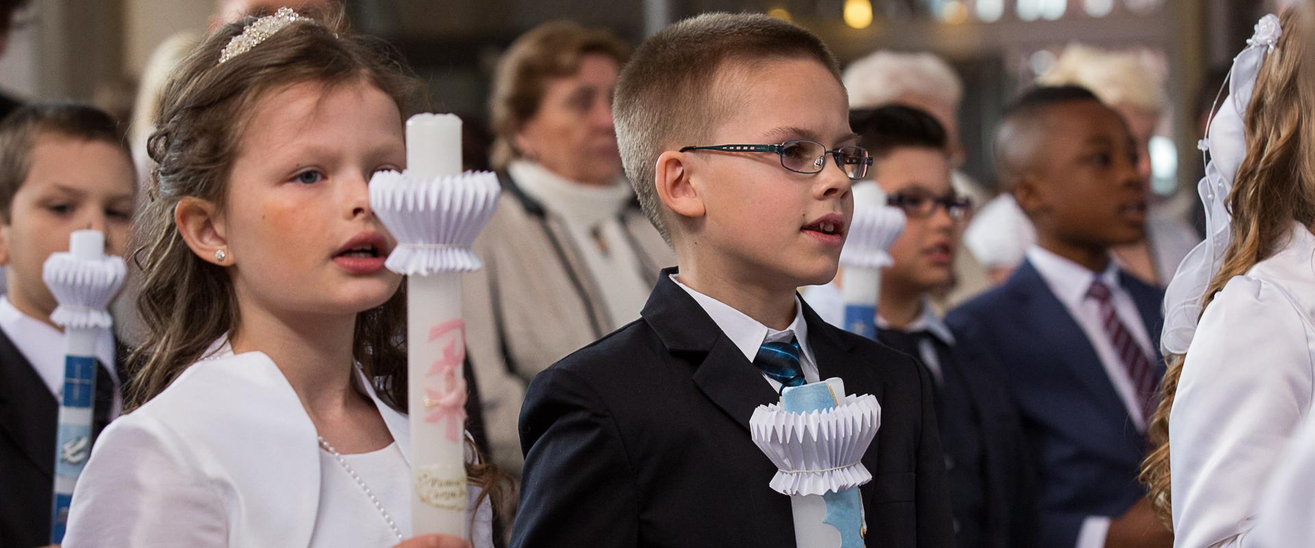 Mehrere Kinder in festlichen Kleidern mit einer Kerze in der Hand.