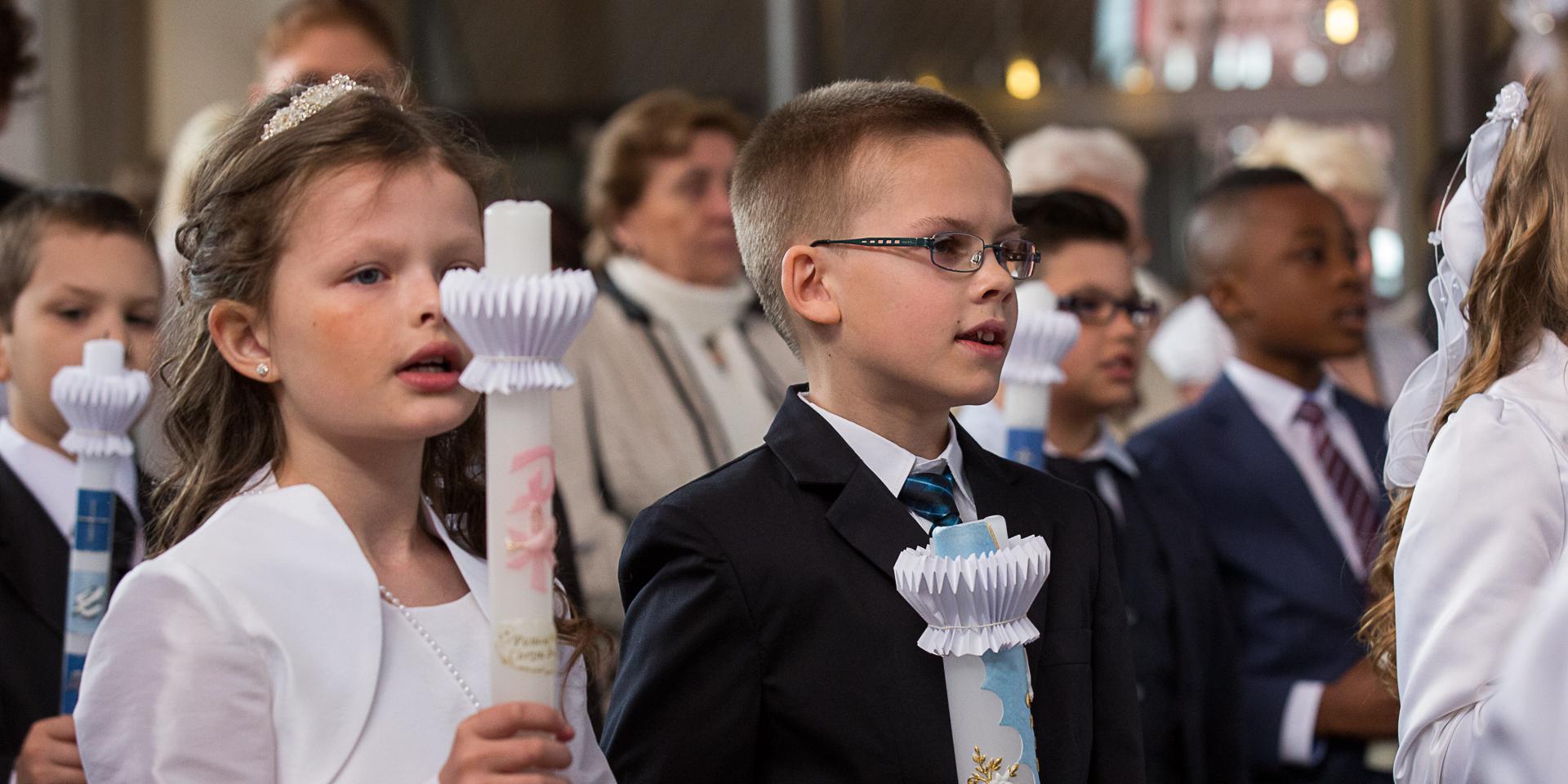 Mehrere Kinder in festlichen Kleidern mit einer Kerze in der Hand.